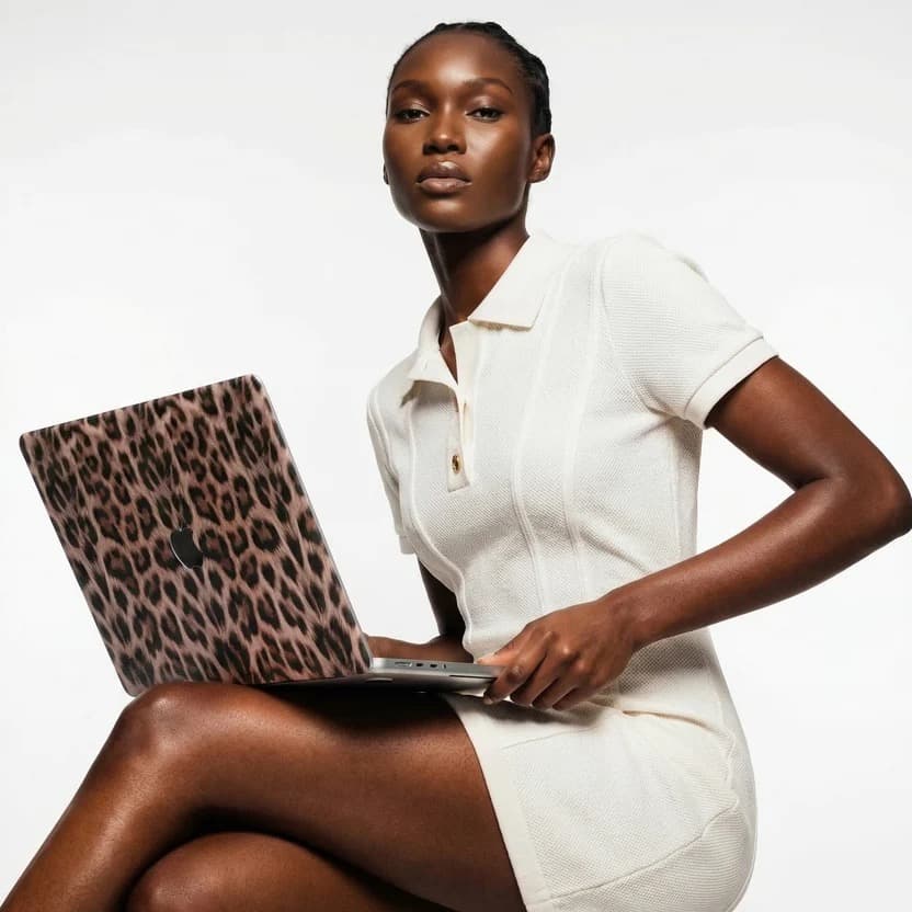 Model holding an open MacBook fitted with the Käel Haus Claudia cheetah-print laptop case